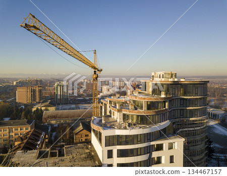 Apartment or office tall building under construction, top view. Tower crane on bright blue sky copy space background, city landscape stretching to horizon. Drone aerial photography. Apartment or office tall building under construction, top view. Tower crane on bright blue sky copy space background, city landscape stretching to horizon. Drone aerial photography. 134467157