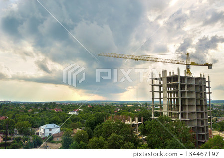 Aerial view of tower lifting crane and concrete frame of tall apartment residential building under construction in a city. Urban development and real estate growth concept. 134467197