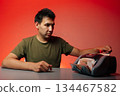 Portrait of serious cashier sitting at desk, counting Russian rubles with electronic money counter machine, studio shot on isolated red background. Concept of financial accounting in dark room. 134467582