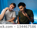 Two young men consuming cake likely containing psychedelic drugs during party at home, showcasing risky and potentially dangerous behavior. Concept of party atmosphere with substance abuse. 134467586