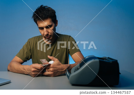 Studio shot portrait of late-night cashier counting banknotes using money counter machine, verifying financial records with precision on isolated background. Concept of illegal cash withdrawal Studio shot portrait of late-night cashier counting banknotes using money counter machine, verifying financial records with precision on isolated background. Concept of illegal cash withdrawal 134467587