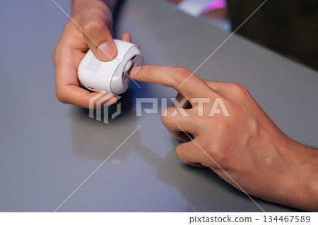 Male hands holding portable electric nail clipper, filing nails on gray table while performing manicure at home using modern beauty tools for grooming and self-care. Concept of healthy lifestyle. Male hands holding portable electric nail clipper, filing nails on gray table while performing manicure at home using modern beauty tools for grooming and self-care. Concept of healthy lifestyle. 134467589