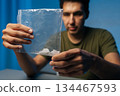 Close-up of of serious drug dealer male preparing dose of cocaine or methamphetamine from plastic bag sitting at table in dark room. Concept of drug dealing or addiction. 134467593