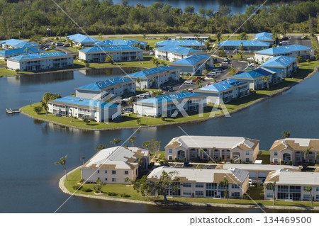 Aerial view of damaged in hurricane apartment building roofs covered with blue protective tarp against rain water leaking until replacement of asphalt shingles 134469500