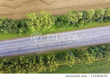 Aerial view of a road between yellow wheat fields and green trees. Aerial view of a road between yellow wheat fields and green trees. 134469530