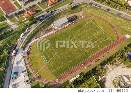 Aerial view of a football field on a stadium covered with green grass in rural town area. 134469533