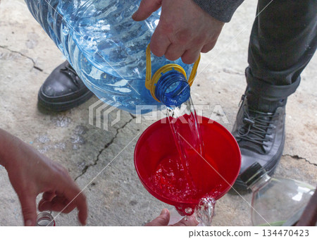 A man pours clean drinking water from a large container into a bottle using a funnel. Close-up. A man pours clean drinking water from a large container into a bottle using a funnel. Close-up. 134470423