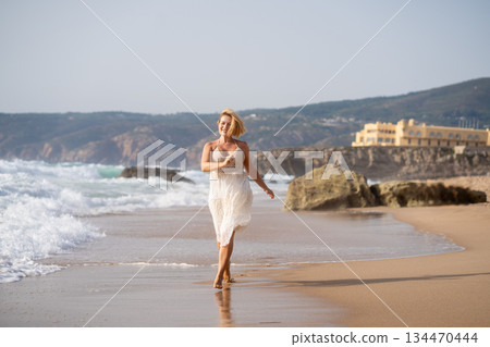Cheerful woman walking barefoot by seaside on Cheerful woman walking barefoot by seaside on 134470444