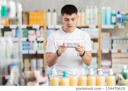 young guy chooses packages of pills in a pharmacy 134470629
