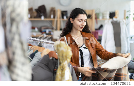 Female shopper chooses and try beautiful checkered coat-jacket in clothing store 134470631