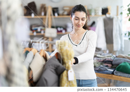 Female shopper selects clothes for autumn winter season in clothing store 134470645