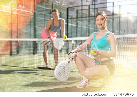 Two young sporty girls getting ready for padel game in court on sunny day Two young sporty girls getting ready for padel game in court on sunny day 134470670