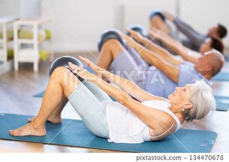 People of different ages doing pilates exercises with fitness ball during group training at fitness studio People of different ages doing pilates exercises with fitness ball during group training at fitness studio 134470678
