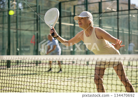 Old woman playing Padel Tennis in open-air tennis court Old woman playing Padel Tennis in open-air tennis court 134470692