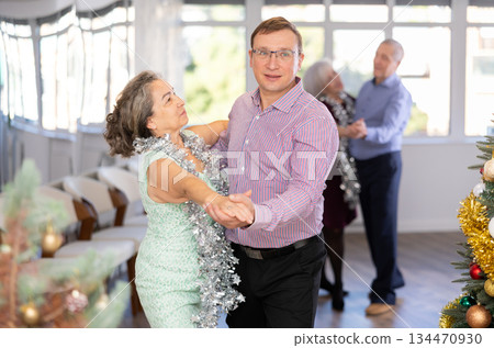 Active middle-aged man and mature woman in pair practicing ballroom dance in training hall during Christmas party 134470930