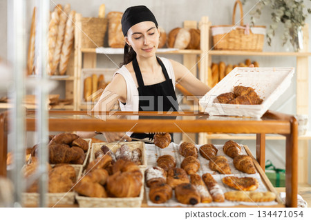 Young woman seller puts croissants in showcase 134471054