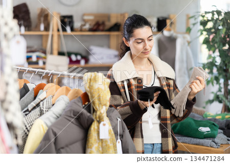 Female shopper carefully selects winter gloves in clothing store. Female shopper carefully selects winter gloves in clothing store. 134471284