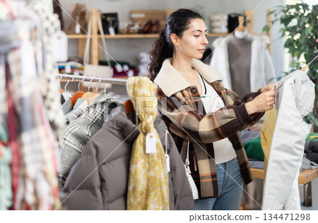 Young woman chooses down jacket in clothing store 134471298