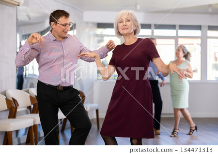 Group of adult active people practicing vogue dancing movements while training twist or rock and roll dance in dance hall Group of adult active people practicing vogue dancing movements while training twist or rock and roll dance in dance hall 134471313
