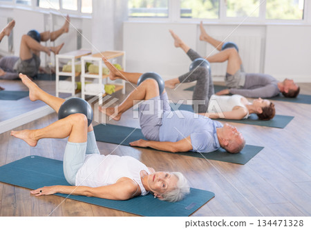 Lying on mat mature woman instructor conducts training with fitball for group students Lying on mat mature woman instructor conducts training with fitball for group students 134471328