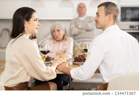 Young couple flirting sitting around table together with old family members looking with objection Young couple flirting sitting around table together with old family members looking with objection 134471367