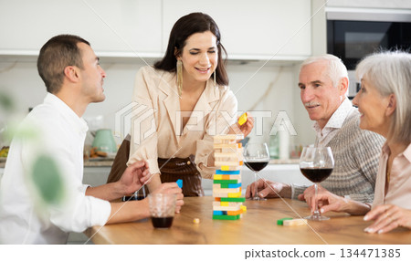 Joyful senior parents and young couple sitting around table playing brick game 134471385