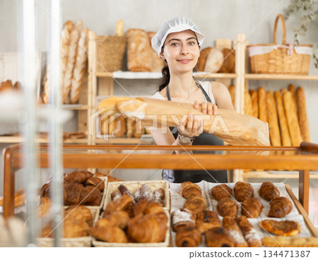Young woman seller took fresh bagguetes of white flour out of window in bakery 134471387