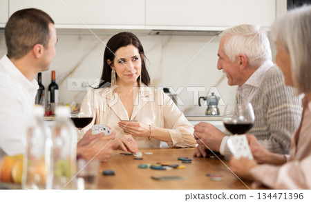 Joyful senior parents and young couple sitting around table playing poker 134471396