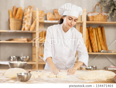 Young woman works as baker, mold baguette from dough, creates long loafs from dough. 134471403