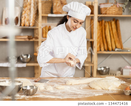 Young woman works as baker, mold buns from dough, creates pastry from dough. Young woman works as baker, mold buns from dough, creates pastry from dough. 134471416