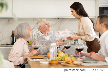 Birthday senior man accepts outright gift and greetings from adult daughter during family feast 134471423