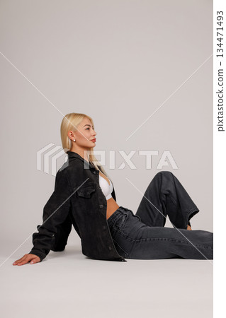 Model sits gracefully in a black denim jacket and jeans 134471493