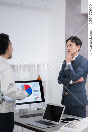 A man in work clothes and a man in a suit are meeting to discuss interior construction and installation work. Is what they're saying different from what's stated in the contract...? 134472600