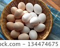 A table bathed in sunlight by the window, with two kinds of fresh eggs served in a colander 134474675
