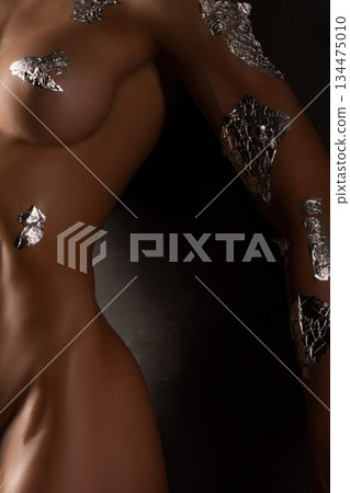 Body art with silver foil applied to skin in a studio setting during a creative session Body art with silver foil applied to skin in a studio setting during a creative session 134475010