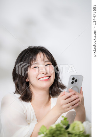 一位快樂、容光煥發的年輕女子正近距離看著她的智慧型手機，搜尋、點擊、看著相機。 134475685