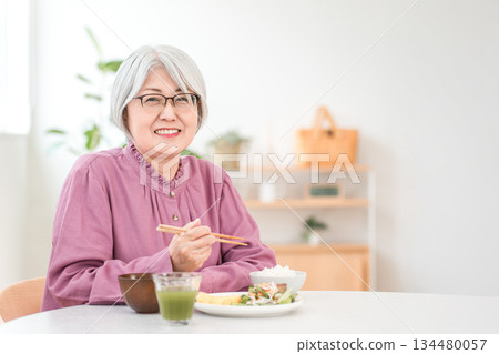 一位白髮老婦人在家裡的餐廳吃飯 134480057