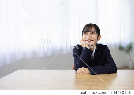 年輕的女商人坐在辦公桌前，手托著下巴，面帶微笑。 134480106