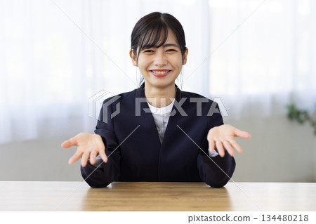 一位年輕的女商人面帶微笑，雙手伸向辦公桌。 134480218