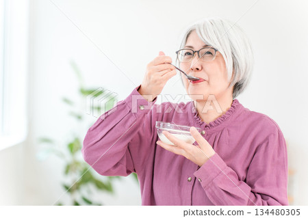 一位頭髮花白的老婦人，她食用優格和乳製品（雙歧桿菌、乳酸菌、乳製品、腸道健康）。 134480305