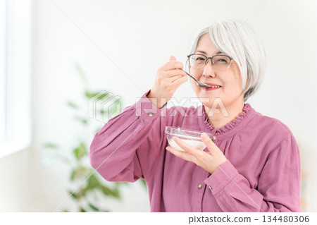 A senior woman with gray hair who eats yogurt and dairy products (bifidobacteria, lactic acid bacteria, dairy products, gut health). A senior woman with gray hair who eats yogurt and dairy products (bifidobacteria, lactic acid bacteria, dairy products, gut health). 134480306