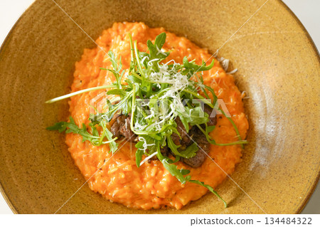 Orange Rose Risotto Topped with Seared Steak Slices and Fresh Arugula in a Gold Bowl 134484322