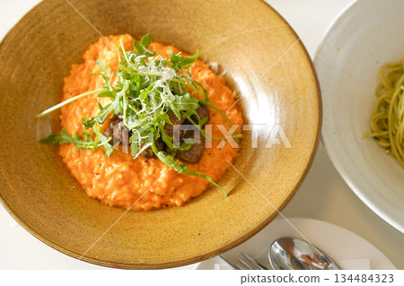 Orange Rose Risotto Topped with Seared Steak Slices and Fresh Arugula in a Gold Bowl 134484323