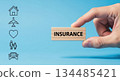 Hand holding wooden block with the word insurance, surrounded by icons representing various types of coverage, emphasizing financial protection and security 134485421