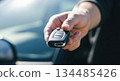 Hand holding car key fob with modern vehicle in background, symbolizing convenience and freedom of car rental services for travelers 134485426