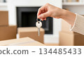 Hand holding house key in front of cardboard boxes, symbolizing new beginnings and the excitement of moving into a rental home 134485433