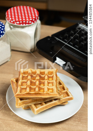 Stack of Homemade Viennese Waffles on a Table with an Electric Waffle Maker 134485864
