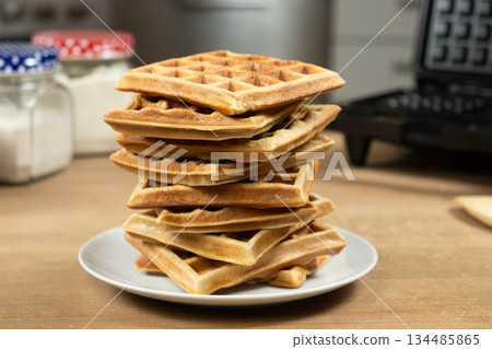Stack of Homemade Viennese Waffles on a Table with an Electric Waffle Maker 134485865