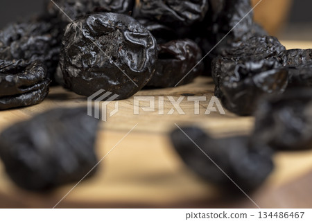 black soft dehydrated fruits of black plums, prunes scattered on the kitchen table, sweet seedless prunes scattered on the table 134486467