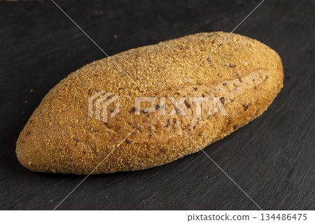 a soft loaf of bread on black slate, a freshly baked soft loaf of rye bread lies on the table a soft loaf of bread on black slate, a freshly baked soft loaf of rye bread lies on the table 134486475